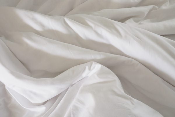 Closeup of beautiful white shiny crumpled polyester fabric sheets on the bed with warm motion and feeling for background and decoration Cloth washing and laundry concept at home